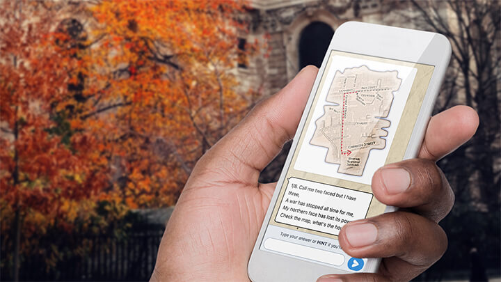 A hand holding a phone playing Treasure Hunt Sheffield with a tree with orange leaves behind.